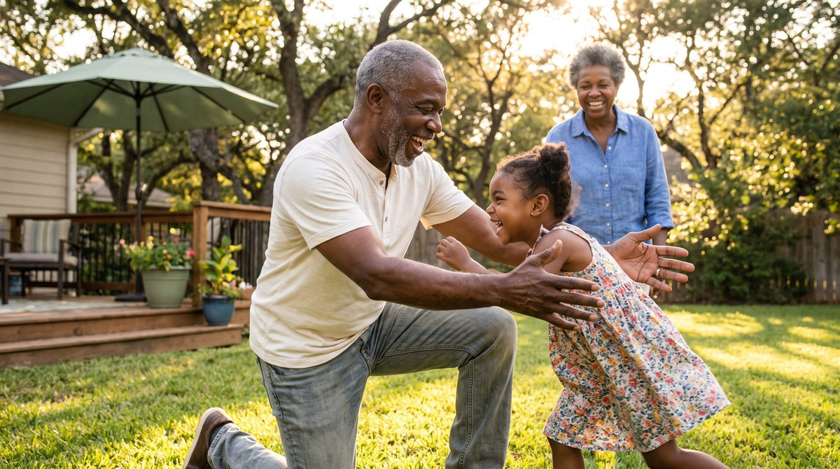 Grandfather kneeling on the lawn catching his laughing granddaughter